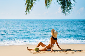 Young beautiful woman sunbathe and relax sitting alone on tropical beach