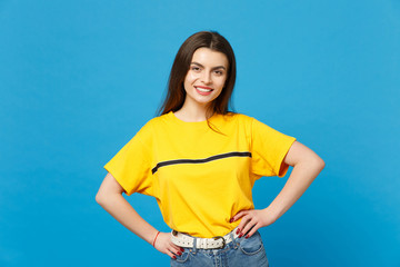 Portrait of smiling attractive young woman in vivid casual clothes standing with arms akimbo on...