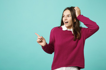 Young brunette smiling woman girl in casual clothes posing isolated on blue green wall background studio portrait. People sincere emotions lifestyle concept. Mock up pointing finger hand on copy space