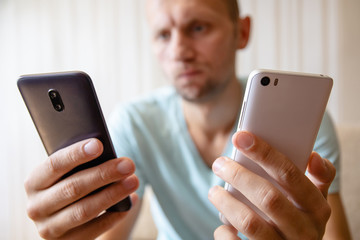a guy with two smartphones in his hands chooses looking at them