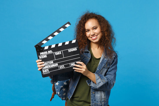 Young african american girl teen student in denim clothes, backpack hold clapper isolated on blue background studio portrait. Education in high school university college concept. Mock up copy space.