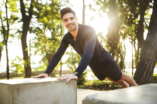 Portrait of caucasian athletic man doing push-ups and stretching his body while working out in sunny green park