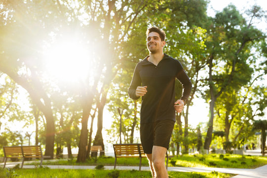 Portrait Of Attractive Athletic Man Running While Doing Workout In Sunny Green Park