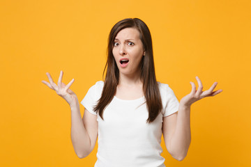 Portrait of bewildered concerned young woman in white casual clothes spreading hands looking camera isolated on bright yellow orange background in studio. People lifestyle concept. Mock up copy space.