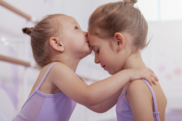 Cropped close up of adorable little ballerina girl kissing her older sister on the forehead....