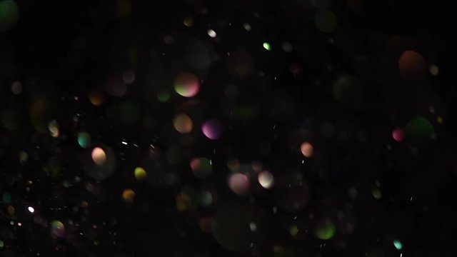 Abstract glittering particles floating bokeh. Colorful blurred dust sparkles on black background. Holiday backdrop. Slow motion 4K UHD video footage. 3840X2160