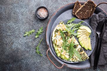 Omelette with avocado and arugula on gray ceramic plate on stone background, top view. Healthy breakfast.