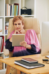 Fototapeta na wymiar Aged businesswoman leaning back on her chair and reading e-book about time management