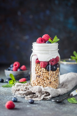 Granola Parfait with Yogurt, oat granola, fresh berries, honey and mint leaves in tall glass jar, copy space