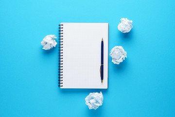 Open notebook, pen and crumpled paper balls on blue background. - obrazy, fototapety, plakaty