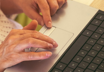 The hands of a caucasian old woman with natural manicure and  touchpad of a notebook. Close-up. Know more about modern technologies. Black keyboard