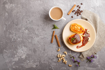 Cheese pancakes with caramel sauce on a beige ceramic plate and a cup of coffee on a gray concrete background. top view.