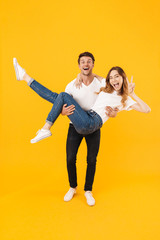 Full length portrait of beautiful couple in basic t-shirts standing together while man picking up...