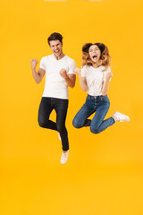 Fototapeta na wymiar Full length portrait of joyful couple man and woman in basic t-shirts rejoicing while clenching fists
