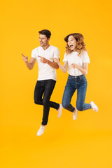 Full length portrait of happy couple man and woman in basic t-shirts smiling while pointing fingers aside at copyspace