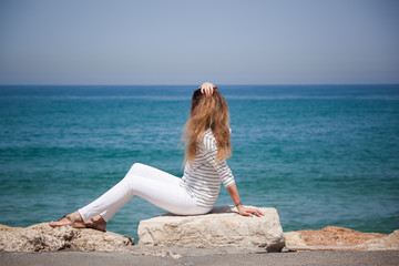 Fototapeta na wymiar happy european girl sitting on a stone by the sea