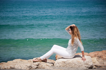 happy european girl sitting on a stone by the sea