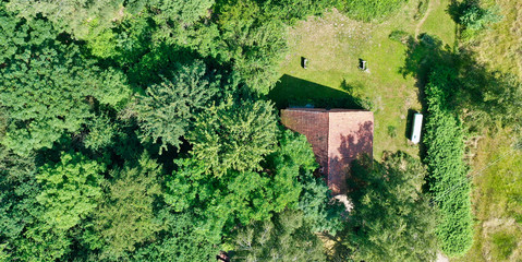 Aerial view from a vertical perspective of a small shed at the edge of a forest with a meadow in front of it.