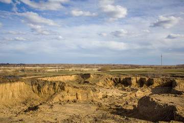 excavated yellow clay quarry on the background of a spring forest landscape under a gray blue sky
