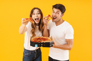 Portrait of cheery couple man and woman in basic t-shirts smiling while eating pizza from box