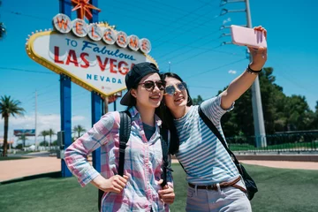 Photo sur Plexiglas Las Vegas Deux amies drôles prenant selfie par téléphone intelligent à l& 39 extérieur dans la rue au soleil avec la lumière du soleil en arrière-plan. Les routards de voyage des dames du groupe font un autoportrait avec un signe de bienvenue à Las Vegas.