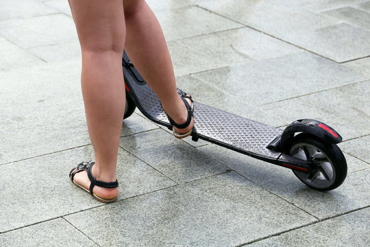 Girl with electric scooter after rain, naked legs in sandals on a sidewalk.  Riding motor scooter on a street, rainy weather in a summer city Stock-foto  | Adobe Stock