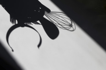 The shadow of a still life of kitchen accessories (spoon, ladle, whisk, grip). Soft focus. High contrast. Copy space