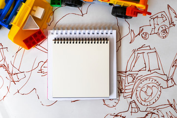  White notepads surrounded by a toy multi-colored dump truck and a tractor with plastic cubes in the background illustration with a tractor. Concept banner. Mockup. Top view. Flat lay. Copy space