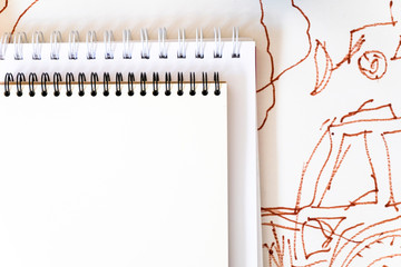 Mockup image: a notebook on a spiral with white square sheets on the background of a picture with tractors and abstractions, which is hand-drawn with markers. Kid's style drawing. Coping space 