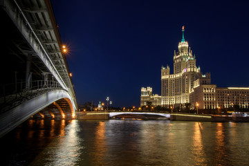 Fototapeta na wymiar View of night Moscow. Stalin-era skyscraper and bridge over the Moscow river illuminated by lights against the dark sky.