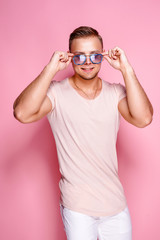 Positive young male in trendy outfit posing against pink background