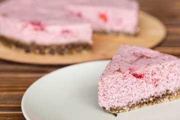 a piece of tasty dessert of light red color with strawberries standing on a plate on the background of a whole cake