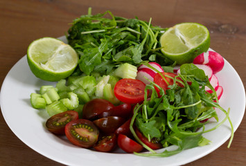 Fresh vegetables as tomato, radish, sliced celery, rosemary and lime on white plate
