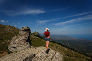 Fototapeta premium The concept of overcoming, rest and freedom. A woman with tanned legs is standing on top with her arms wide open on either side. Near the rocks of unusual shape. 