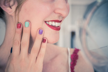 Attractive red lip stick: Blonde young woman with colorful nail polish is looking herself in the mirror. Cut out of the face.