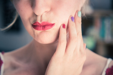 Fototapeta premium Attractive red lip stick: Blonde young woman with colorful nail polish is looking herself in the mirror. Cut out of the face.