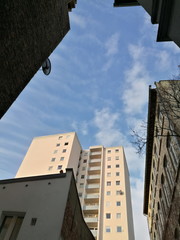Blick aus einem engen Hinterhof auf ein saniertes Hochhaus in Pastellfarben bei blauem Himmel und...