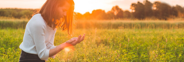 Teenager Girl closed her eyes, praying in a field during beautiful sunset. Hands folded in prayer...
