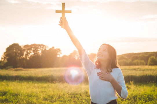 Teenager Girl holding a the cross in hand during beautiful sunset. Hands folded in prayer concept for faith, spirituality and religion. Peace, hope, dreams concept