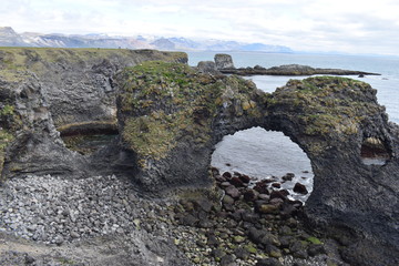 Hiking trail from Anarstapi to Hellnar with the raw ocean und big rocks and mountains and a stone gate in the west of Iceland at Snaefellsnes Peninsula