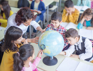 teacher and a group of students examines world map in lecture with magnifying glass