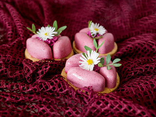 Three delicious pink cakes decorated with white flowers and green leaves on burgundy fabric. Dessert