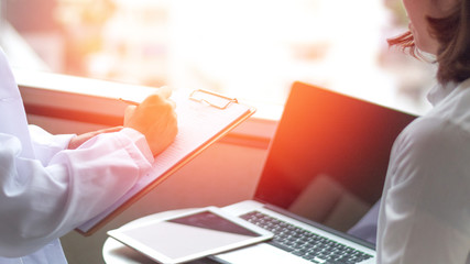 Professional medical doctor in white uniform gown coat interview counseling female patient: Physician writing on patient chart while consultation: Hospital/ clinic healthcare professionalism concept