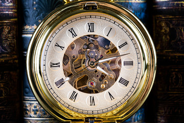 Antique clock on the background of vintage books. Mechanical clockwork on a chain.