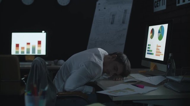 Tired businessman sleeping on work table front computer in dark office.