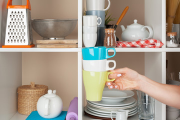 Woman hand taking dishware pieces from shelf in kitchen