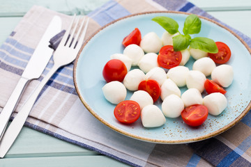 Delicious caprese salad with ripe cherry tomatoes and mini mozzarella cheese balls with fresh basil leaves.