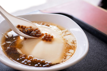 Popular Taiwan gourmet - Dessert of tapioca pearl ball (bubble) mixed bean curd tofu pudding (douhua, dou hua) in white bowl, close up, lifestyle