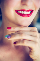 Obraz premium Attractive red lip stick and healthy white teeth: Blonde young woman with colorful nail polish is looking herself in the mirror.