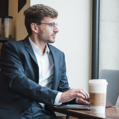 Young businessman using laptop in cafe looking away